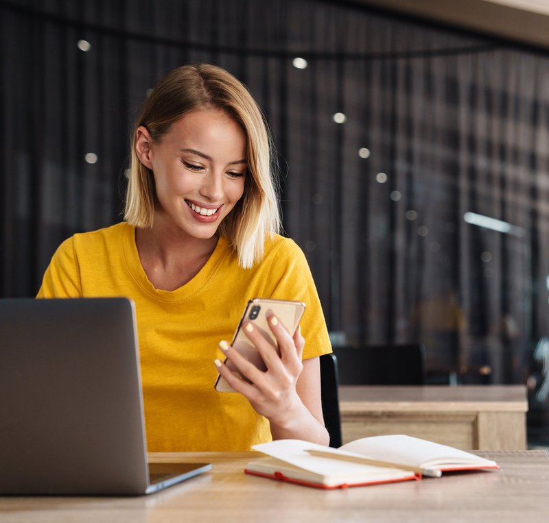 Security360 Bild - Frau mit Mobile Frau mit mit gelbem Shirt loggt sich an einem Computer ein mit Hilfe ihres Mobiles