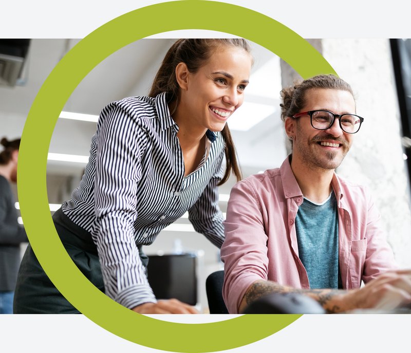 Workplace360 Titelbild Zwei fröhliche Mitarbeitende vor einem Computer